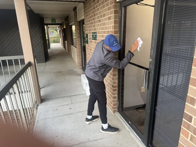 A Higeniks cleaner wiping the glass of a building entrance door.