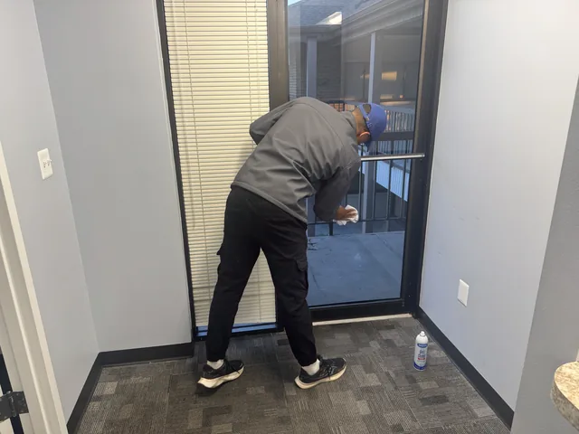 A Higeniks cleaner wiping down the interior glass door of an office suite.